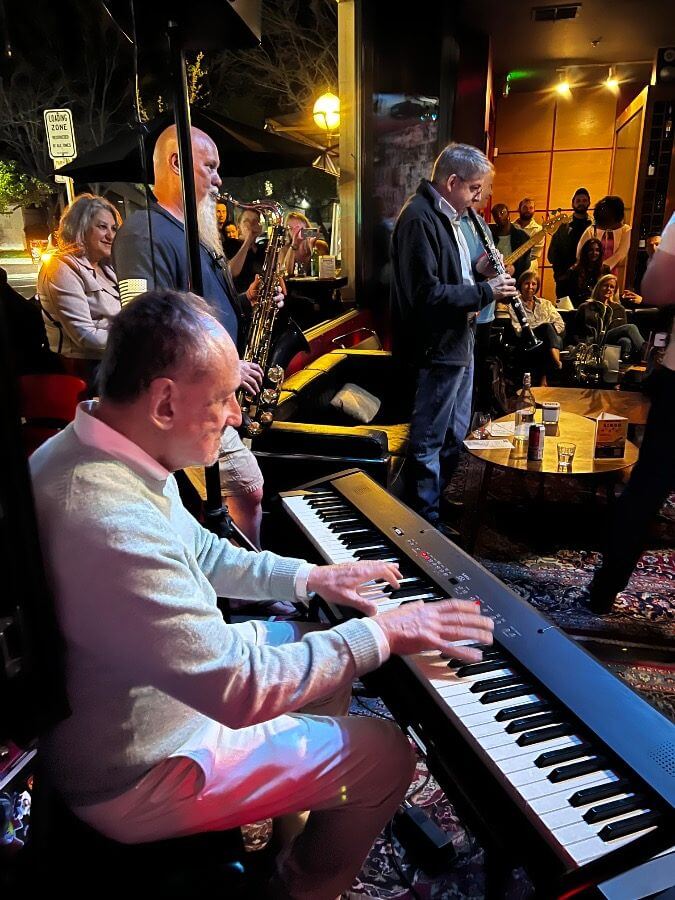 A pianist and horn players at an evening jam session